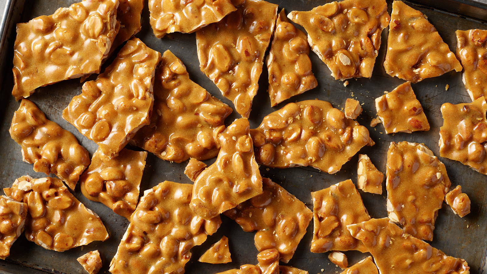 Broken up pieces of peanut brittle on a baking sheet.