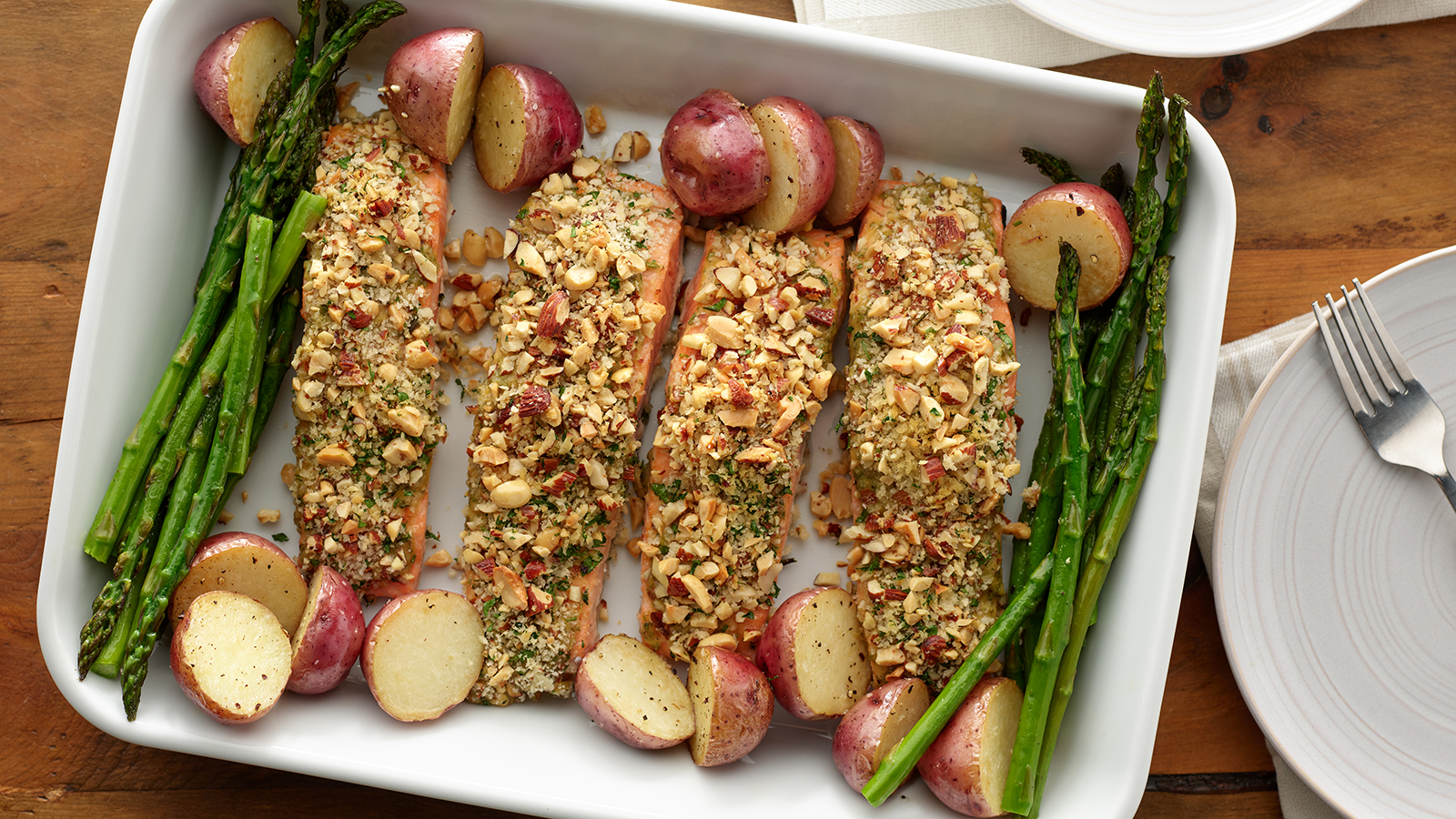Mixed nut crusted salmon with roasted asparagus and potatoes in a baking dish.