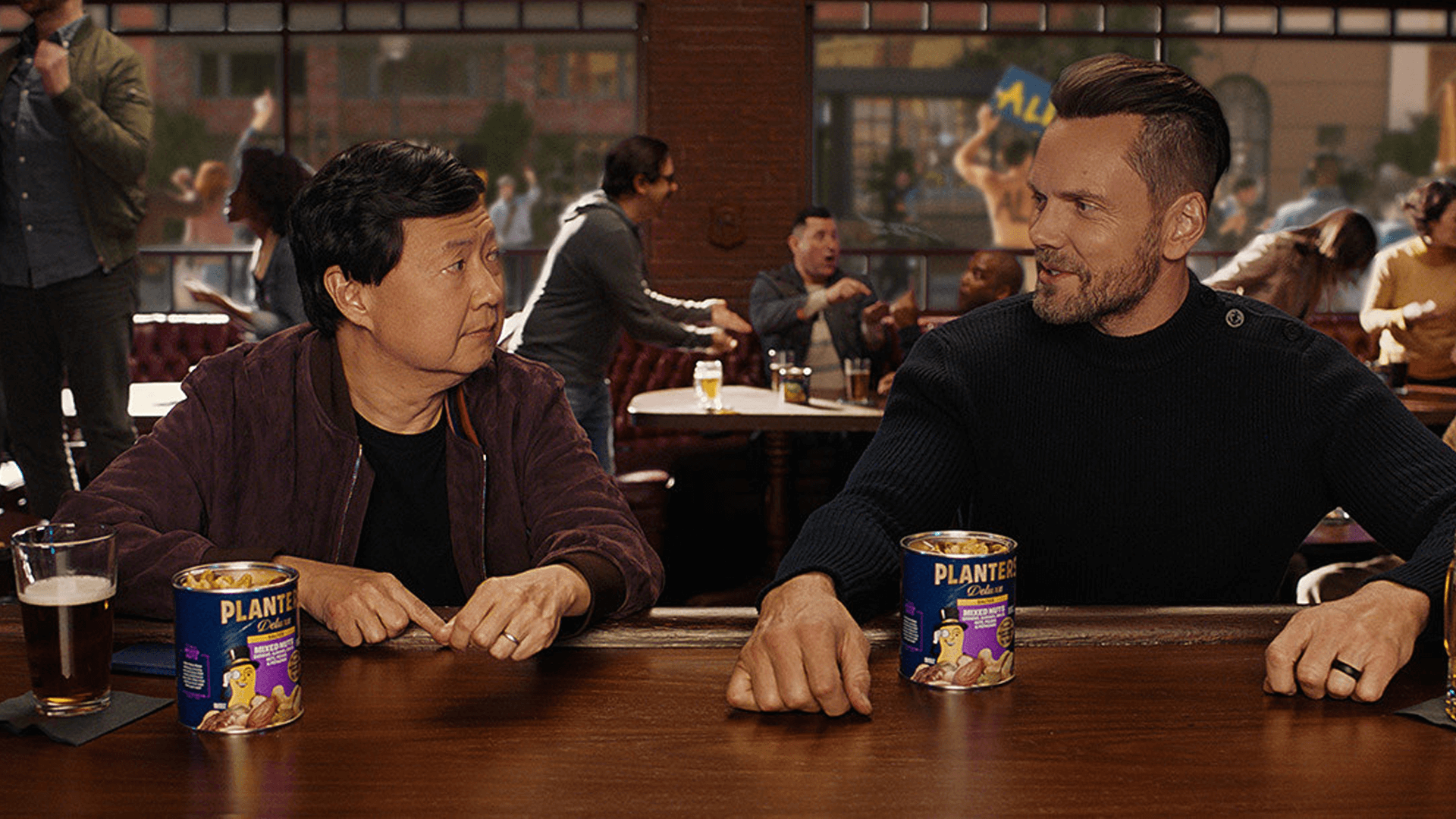 Two men sitting at a bar eating planters nuts