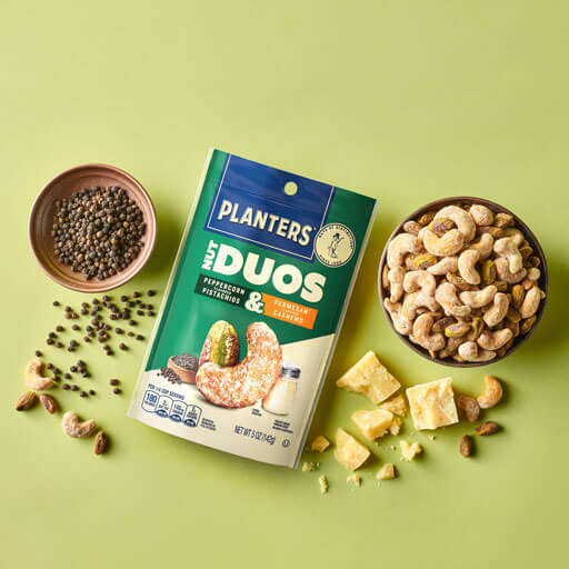 Promotional photo of planters duos peppercorn pistachios and parmesan cashews with a charcuterie board on a green background
