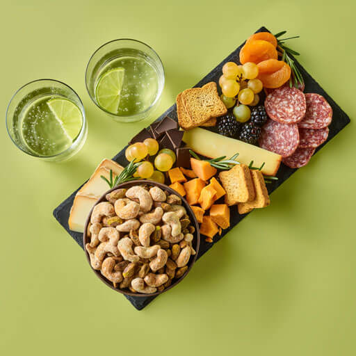 Promotional photo of planters duos peppercorn pistachios and parmesan cashews with a charcuterie board on a green background