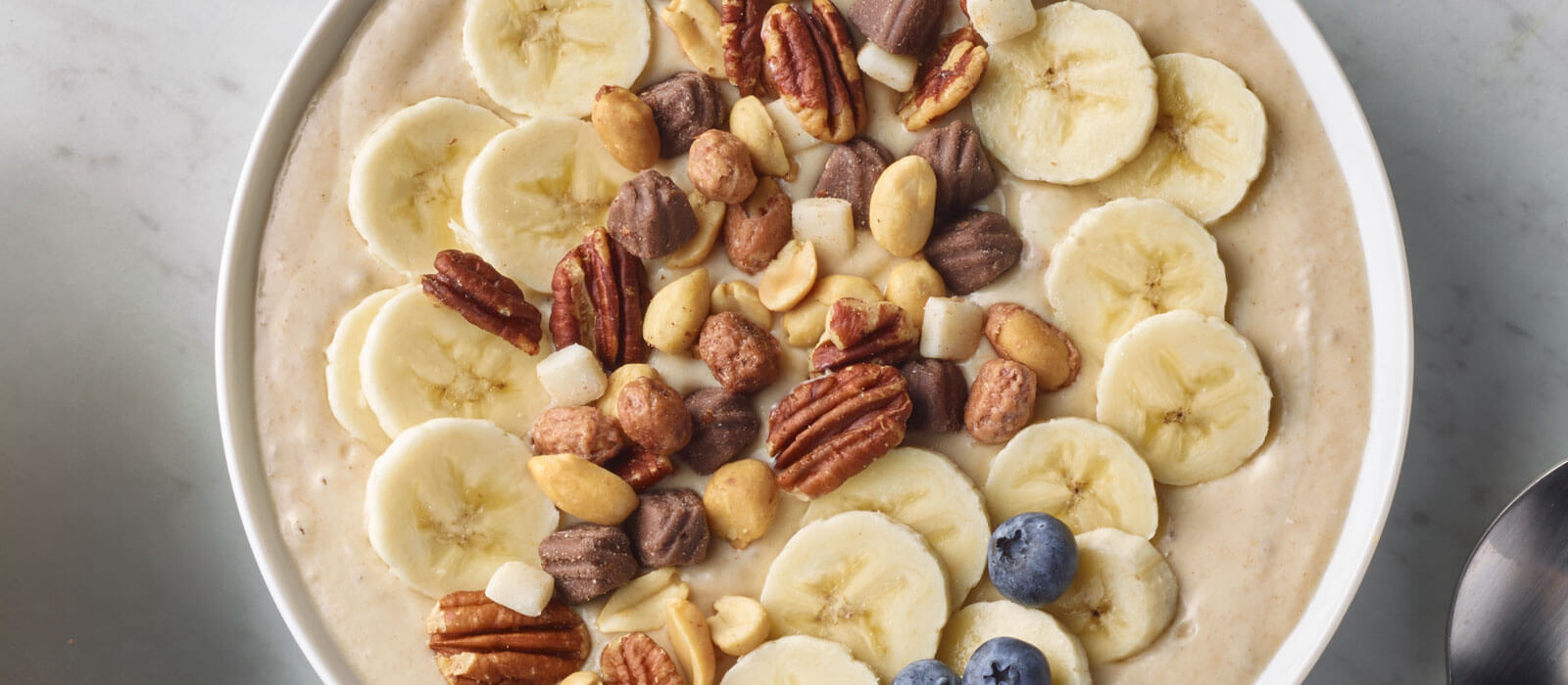 Overhead view of a smoothie bowl topped with bananas and trail mix