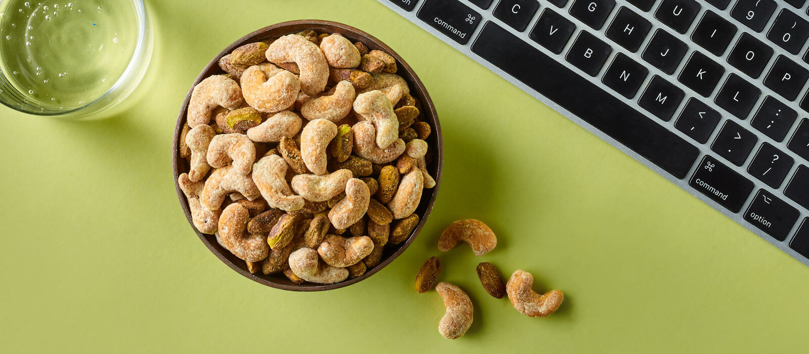 Overhead view of Nut Duos peppercorn pistachios and parmesan flavored cashews in a bowl with a green background
