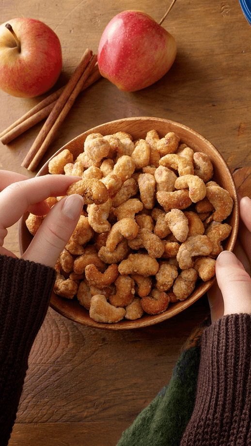 Apple cider cashews in a bowl on the counter with apples