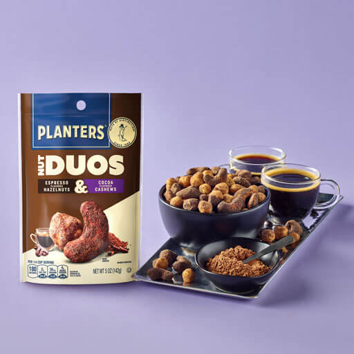 Planters duos espresso hazelnuts and cocoa cashews promotional photo on a snack board with a purple background